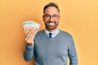 © Krakenimages.com - Handsome middle age man holding bunch of 50 euro banknotes looking positive and happy standing and smiling with a confident smile showing teeth