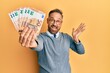 © Krakenimages.com - Handsome middle age man holding bunch of euros celebrating achievement with happy smile and winner expression with raised hand