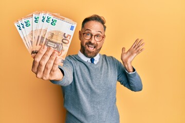 Sticker - Handsome middle age man holding bunch of euros celebrating achievement with happy smile and winner expression with raised hand