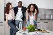 © sofiko14 - Happy joyful mixed race teen girl showing to the camera pieces of cucumber, while making fresh salad in the kitchen. Smiling multiracial parents standing on the background
