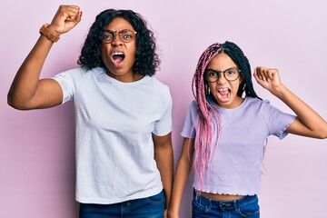 Canvas Print - Beautiful african american mother and daughter wearing casual clothes and glasses angry and mad raising fist frustrated and furious while shouting with anger. rage and aggressive concept.