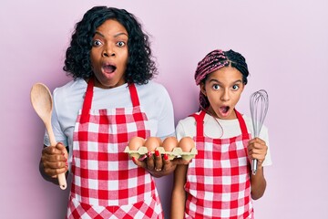 Wall Mural - Beautiful african american mother and daughter cooking cake using baker whisk afraid and shocked with surprise and amazed expression, fear and excited face.