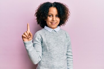 Sticker - Young little girl with afro hair wearing casual clothes smiling with an idea or question pointing finger up with happy face, number one