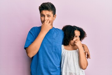 Sticker - Young hispanic family of brother and sister wearing casual clothes together smelling something stinky and disgusting, intolerable smell, holding breath with fingers on nose. bad smell