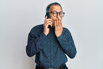 Poster - Middle age indian man having conversation talking on the smartphone covering mouth with hand, shocked and afraid for mistake. surprised expression