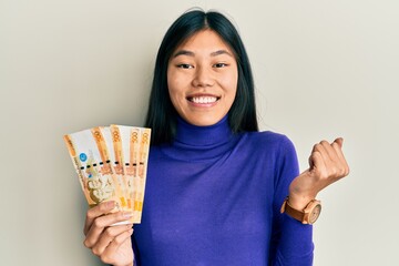 Wall Mural - Young chinese woman holding 500 philippine peso banknotes screaming proud, celebrating victory and success very excited with raised arm