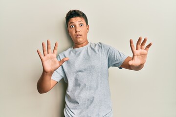 Teenager hispanic boy wearing casual grey t shirt afraid and terrified with fear expression stop gesture with hands, shouting in shock. panic concept.