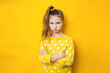 Dissatisfied offended sad teenager girl with arms crossed on yellow background with copy space