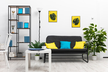 A large bright living room in the house with black furniture and accessories in blue and yellow. Modern interior design of the apartment.