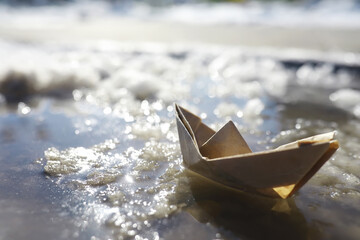 Paper boat in the water on the street. The concept of early spring. Melting snow and an origami boat on water waves.