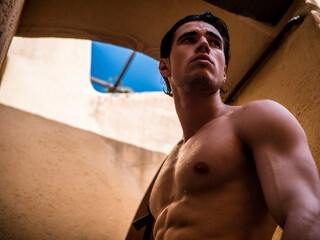 Wall Mural - Handsome muscular shirtless man posing in old town alley in Italian town in summer. Horizontal outdoors shot