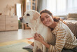 © Seventyfour - Warm toned portrait of smiling young woman embracing dog while sitting on floor and enjoying time with loving pet, copy space