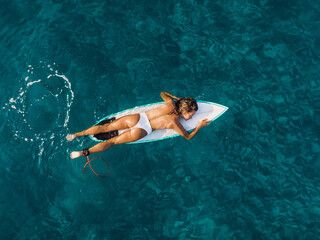 Wall Mural - Attractive surfer woman relaxing on surfboard in ocean. Aerial view with surf girl