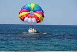 Fototapeta  - różnokolorowy, tęczowy spadochron ciągnięty przez motorówkę na tle lazurowego morza śródziemnego