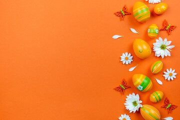 Wall Mural - Easter eggs, white spring flowers and butterflies on colorful orange background. Holiday Flat lay concept. Traditional springtime decoration. Top view. Copy space.