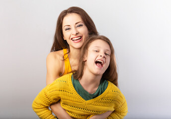 Wall Mural - Happy laughing mother and excited shouting kid girl hugging together on blue light background. Closeup