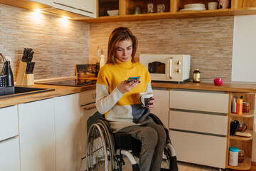 Wall Mural - Female in wheelchair drinking coffee and using phone at home