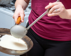 One hand holds the pan, the other pours the dough with a ladle. Preparation for the celebration of Maslenitsa. Selective focus.