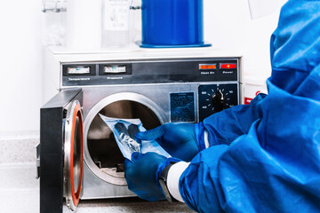 unrecognizable person in bio security suit holding tools and putting them into a machine to sterilize them.