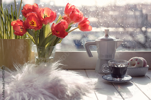 Espresso i glass cup cooked in ceramic coffee maker on window sill. Wooden windowsill with spring flowers, hyacinth and orange tulips. Cozy scene, hygge concept.