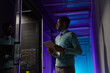 © Seventyfour - Side view portrait of young African American data engineer working with supercomputer in server room lit by blue light, copy space
