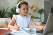© ty - Smiling little girl in headphones handwrite study online using laptop at home, cute happy small child in earphones take Internet web lesson or class on PC.