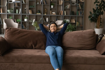 Wall Mural - Happy millennial Indian woman sit relax on comfortable couch in living room sleep or take nap. Calm young mixed race female renter rest on sofa at home, daydream enjoy leisure weekend. Rent concept.