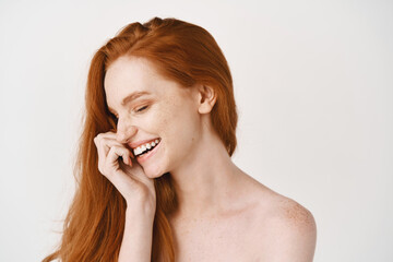 Wall Mural - Beauty. Close-up of happy redhead woman with pale perfect skin, laughing and showing white teeth, standing naked on studio background