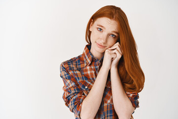 Wall Mural - Cute girlfriend with long ginger hair and pale skin pleading for something, looking at camera with asking expression, standing over white background