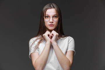 attractive surprised excited scared, terrified teenage girl wear glasses, white t shirt, with brown long hair, isolated on gray background. Concept of human emotions, facial expression, sales, ad.