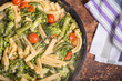 Cooking primavera pasta in a pan - vegan american and italian primavera pasta dish with broccoli, beans, asparagus, peas and tomatoes in a pan on a wooden table, top view