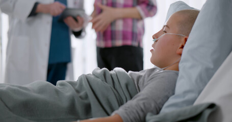 Sick child with cancer lying in hospital bed while mother talking to doctor on background