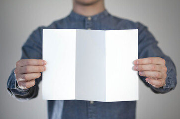 Wall Mural - A man holds a white piece of paper. A flyer in the hands of a man. Prepared for your text. Isolated on a gray background