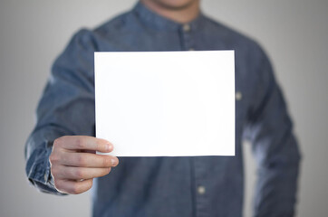 Wall Mural - A man holds a white piece of paper. A flyer in the hands of a man. Prepared for your text. Isolated on a gray background