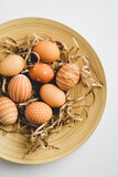 Fototapeta Kwiaty - Easter eggs and straw on plate on white background. Flat lay, top view, vertical