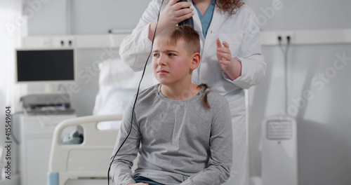 Teenage kid sitting on chair in clinic ward and having haircut © nimito