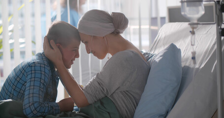 Upset teenage boy embracing sick mother with cancer in hospital