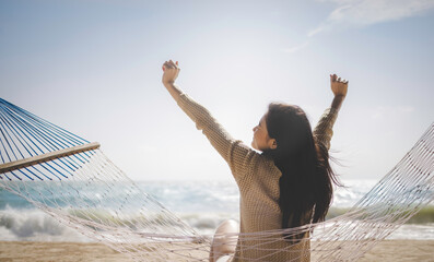 Summer vacation concept, Cheerful asian female tourist stretch arms relaxing sitting on hammock at beautiful beach