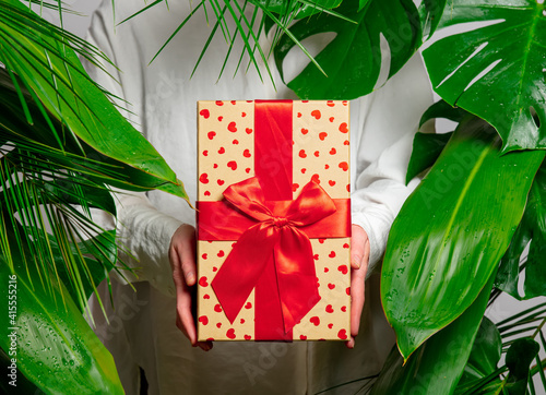 female hand holding gift box on background with palm leaves © Masson