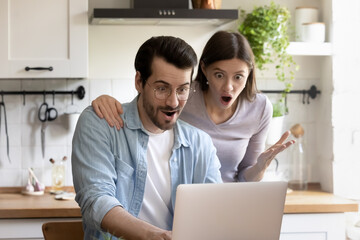 Wall Mural - Shocked millennial Caucasian couple look at laptop screen stunned by unexpected news online. Amazed young man and woman spouses surprised by unbelievable good sale deal or discount offer on computer.