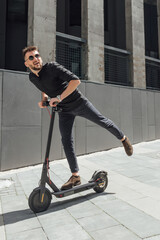 Wall Mural - Young man riding electric scooter in urban background
