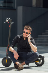 Wall Mural - Young man sitting on  electric scooter with phone in urban background