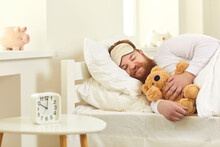 Happy Grown-up Man Sleeping In Good Comfortable Bed With Cute Teddy Bear. Funny Guy Lying On White Pillows And Dreaming Sweet Dreams In Deep Sleep At 10 Am In Covid-19 Lockdown Or On Weekend Morning