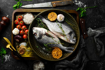 Raw Dorado fish with lemon and thyme in a metal tray. Fish cooking recipe. Top view. Free copy space. On a black stone background.