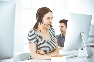 Casual dressed young woman using headset and computer while talking with customers online. Group of operators at work. Call center, business concept