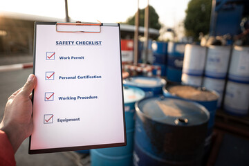 Hand of operation staff is using the safety checklist sheet to verify working condition in chemical storage area (blurred background). Working in unsafe workplace concepts action photo.