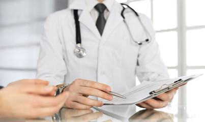 Unknown male doctor and woman-patient discussing current health examination while sitting in clinic and using clipboard. Good medical service in hospital. Medicine concept