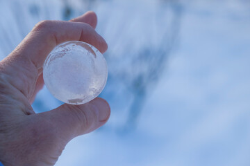 Pure transparent ice sphere in human hands on a blue background. Ecology concept. Copy space. Close up.