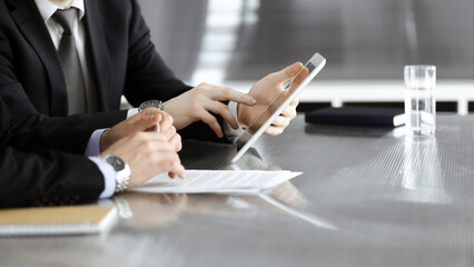 Unknown businessmen using tablet computer and work together at the glass desk in modern office, close-up. Teamwork and partnership concept