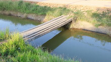 Temporary Bridge Over Water Canal. A Concrete Pillar Bridge For Walking Across The Water In The Way Of Rural Residents And Reflecting The Bridge On The Water With A Copy Area. Selective Focus